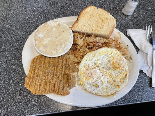 Chicken fried steak with hash browns, eggs over medium, sourdough toast and gravy on the side.