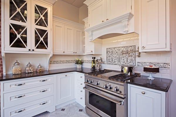 The kitchen cabinetry is painted white, with inset doors. Marble floor, classic subway tile backsplash with decorative accents.