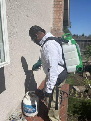 Pest control technician applying treatment around the exterior of a house