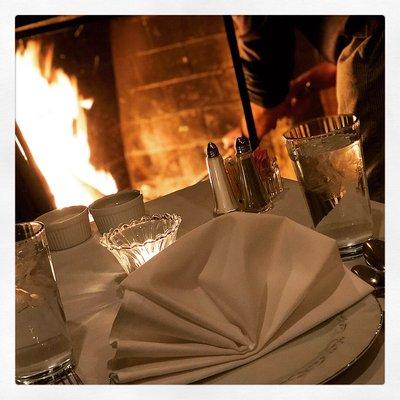 Dining room table set for two in front of a warm fire