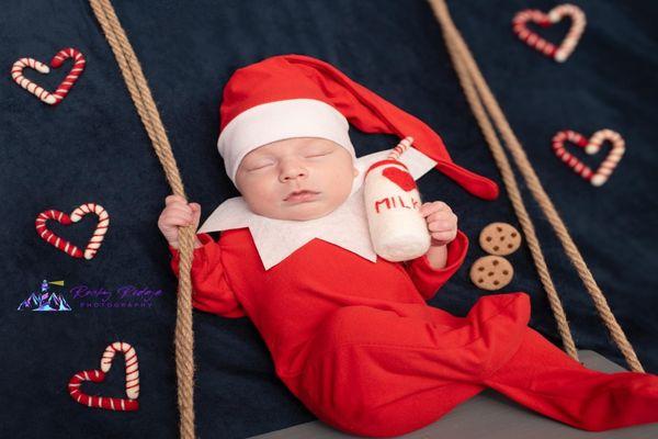 Newborn baby in swing with elf outfit, milk, cookies, candy canes.