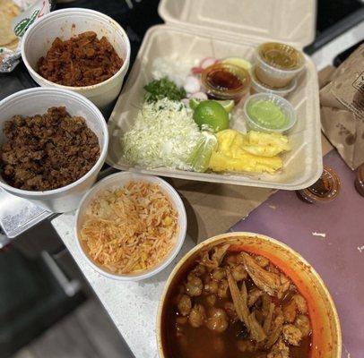 Pozole in the front, family taco pack in the back of photo. Beyond taco meat El Pastor and a toppings box. Chow down!!!