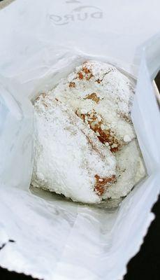 Beignets loaded with powdered sugar in a bag for you to shake.