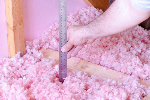 Home insulation contractors measuring the height of blown in insulation within an attic.