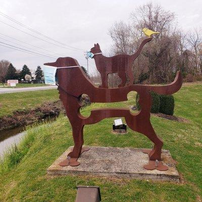 Large statue of a profile of a dog, cat and bird. The dog and cat are wearing surgical face masks.