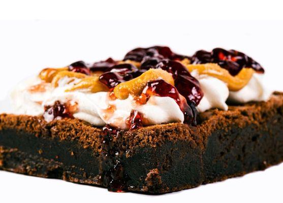 Rediscover the classics with our Peanut Butter and Jelly Brownies, topped with fluffy whipped cream and a medley of sliced strawberries, mar