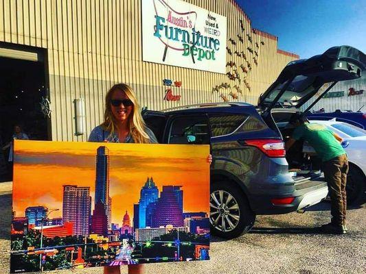 A Happy customer holding a Large Gallery wrapped canvas of the Sunrise SoCo in front of Austin Furniture Depot