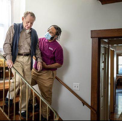 Caregiver helping elderly man downstairs.