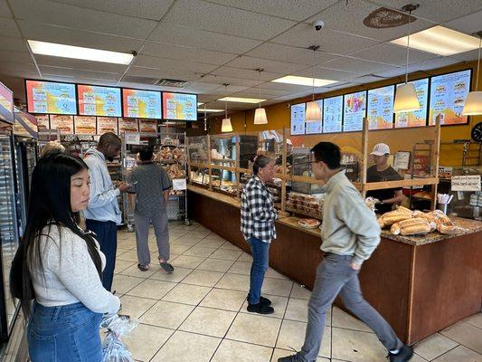 The inside of the bakery with bánh mì menu on screens above the counter