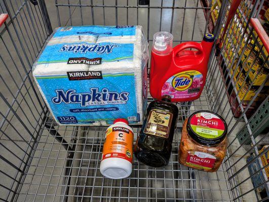 Kirkland Signature Napkins ($11.99), Vitamin C ($14.99), Organic EVOO ($22.59), Tide with Downy ($19.99), and Kimchi ($8.99).