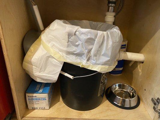 Under sink. Trash, dog bowl, paper towel, aluminum foil, dustpan and brush