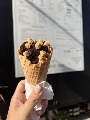 Vanilla soft serve on waffle cone topped with hot fudge and cookie dough