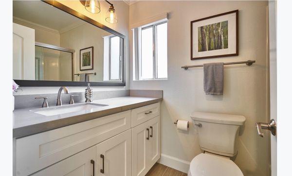 Bathroom cabinets, mystery gray quartz counter, sink, toilet, lights, mirror, sliding shower door, continuous wood like tile flooring.