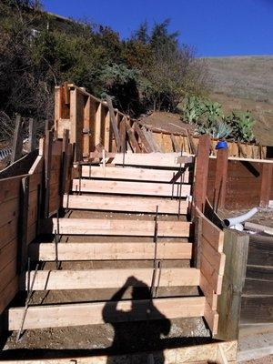 SETTING UP FOR POUR FOR STAIRS WITH A RETAING WALL UP THE BACK OF A YARD WITH LANDSCAPE