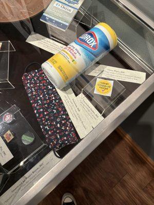 COVID masks, wipes, and vaccination stickers in a glass box alongside the timeline of Tulsa's history