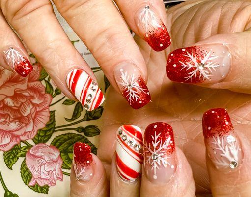 These nails have a fun Christmas look with red glitter, candy cane stripes, snowflakes, and shiny rhinestones. Perfect for the holidays!