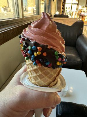 Red velvet soft serve ice cream in waffle cone with chocolate and M&Ms.