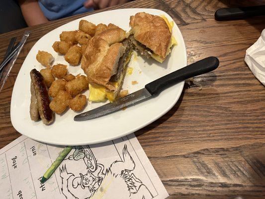 Croissant breakfast sandwich - sausage, egg, and cheese with a side of tater tots.