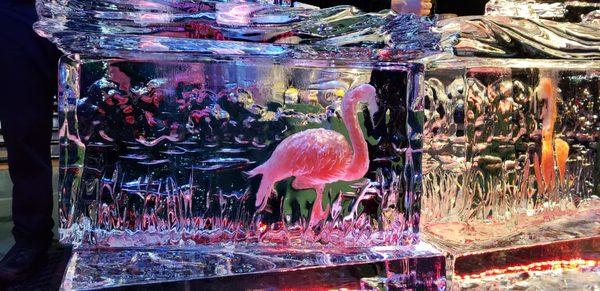 A colored  flamingo carved into the ice to make a beautiful carving. This block of ice is part of an ice bar which was used to serve drinks.