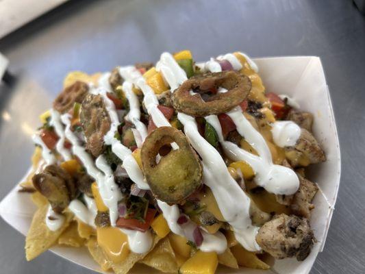 Jerk Chicken Nachos. Warm tortilla chips topped with melted cheese, jerk chicken, mango Pico, lime crema, and fried jalapenos.