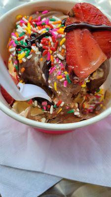 Cake, banana and chocolate topped with sprinkles, strawberries and fudge