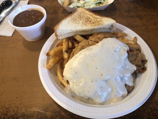 Chicken fried steak with beans and French fries as sides.