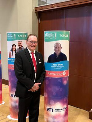 Tom Grady (owner) at ATI Super Conference 2023  and standing next to his Top 25 ATI Shop photo