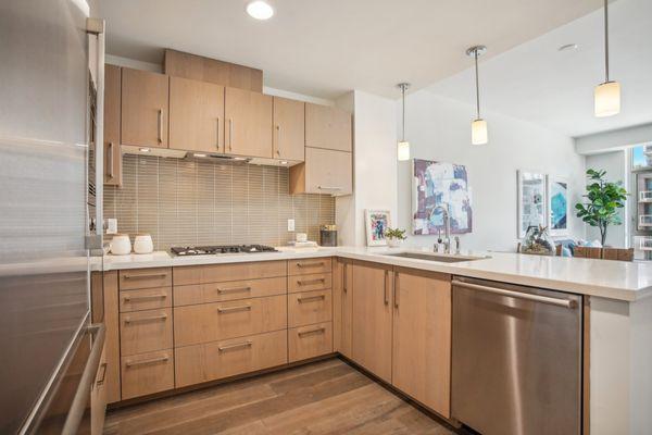 Modern kitchen with light wood cabinets, stainless steel appliances, white countertops, and pendant lighting.