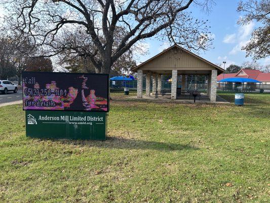 Park sign with covered picnic tables, and pool in the background.