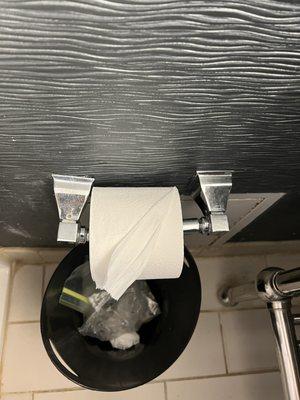 Toilet paper holder falling off wall and trash in waste basket