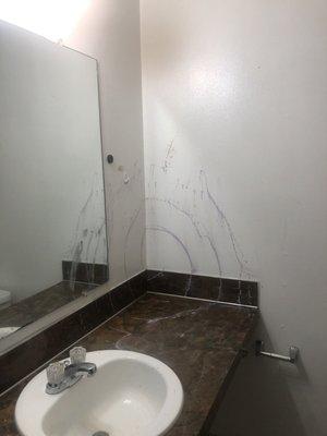 Purple paint and makeup splattered all over the bathroom walls and mirror.