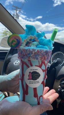 A cotton candy milkshake with cotton candy crumbles, lollipop and cotton candy on top.