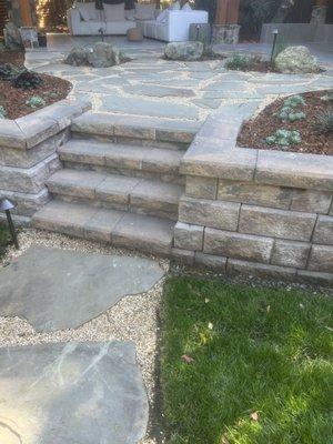 Entrance of retaining wall to the top patio area. Stone walkway with lights and planter areas around