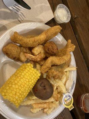 Fried fish and fried shrimp with corn, potatoes, and fries.