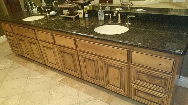 Granite countertop, knotty alder cabinets and travertine flooring with two sinks and faucets.