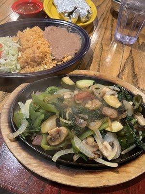 Sizzling vegetarian fajitas with beans, rice, and tortillas on the side.