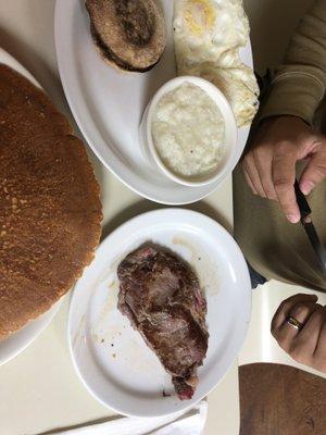 Steak and eggs platter with English muffin and grits. With side of banana pancakes