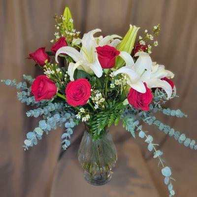 Red roses oriental lilies and spiral eucalyptus arranged in clear glass vase