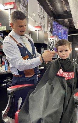 Carlos, a classically styled barber giving my son a cut.