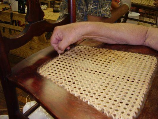 a student at work finishing a hand-cane chair seat during our thursday evening class