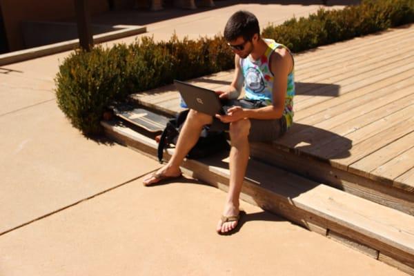 A student fires up his laptop to check in on online classes while taking in some sun.