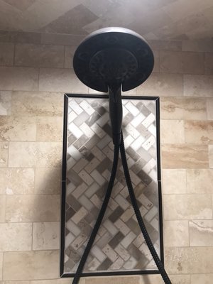 Travertine shower walls with a stone mosaic inset in a herringbone pattern.