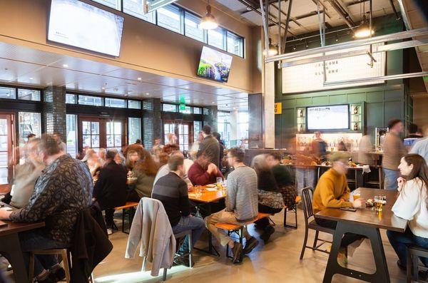 A bustling bar with patrons at tables, at SLU BRU. Enjoy drinks, games, and popcorn!