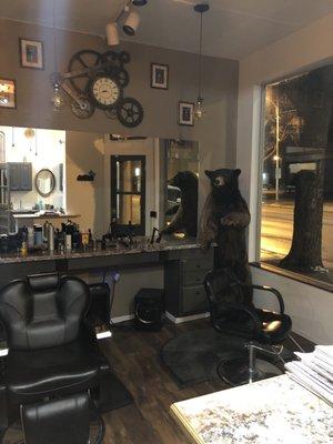 There are two barber chairs , A bear standing and a very big window