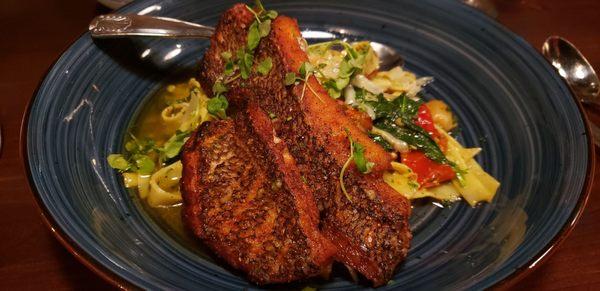 Special pan seared bass over fettuccine pasta in a pesto white wine sauce with tomatoes, spinach, roasted garlic