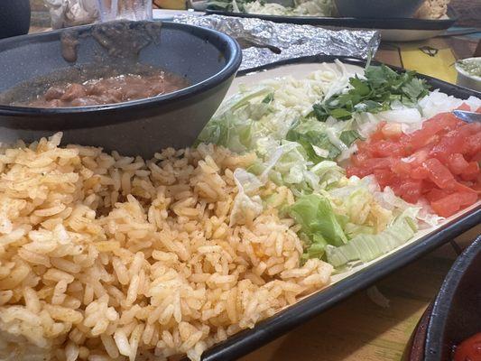 Spanish rice, refried beans and 'salad' as it's called. Tortillas wrapped in foil can be seen in the background.