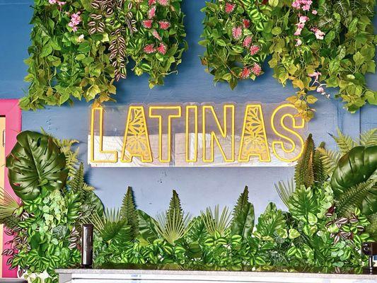 Latinas LED neon sign and greenery greeting you as you enter.