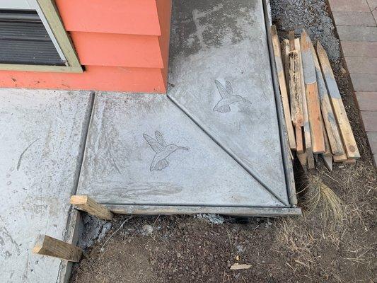 Concrete skirt around shed with stamped hummingbird.