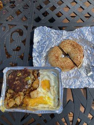 Breakfast plate with sunny side eggs, sausage patty, home fries with onion & pepper, and a grilled onion bagel!