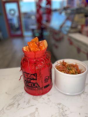 Ice cold Agua Fresca with salsagheti candy, chopped fruit, chamoy, and your choice of chips in the compartment below